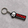 Titan Scaffolding custom keychain with white helmet icon, red TITAN lettering, silver chain and keyring on a textured gray concrete surface.