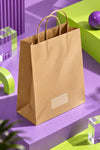 A brown kraft paper shopping bag with twisted paper handles and a blank white label window on the front, styled on purple and lime green geometric platforms.