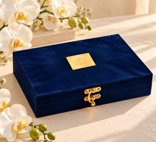Navy blue velvet gift box with gold plaque and clasp on cream surface with white orchids