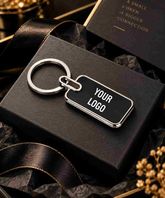 A customizable black rectangular keychain with a silver metal border, key ring, and split ring, displayed on a black gift box with a black ribbon.