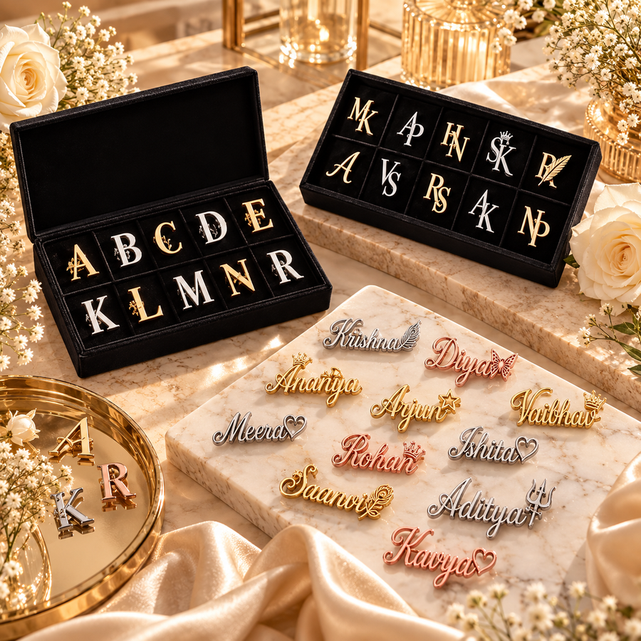 A–Z monogrammed apparel accessories in gold, silver and rose-gold finishes displayed in black velvet presentation boxes on a luxury marble setting with elegant floral and satin accents.