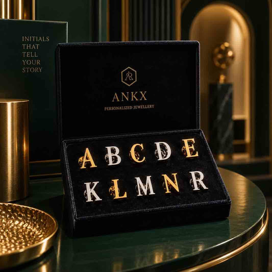A personalized lettering jewelry set displayed in a black velvet box on a dark green table. The set includes gold and silver letter pieces spelling out A through R, with decorative floral accents on the gold letters.