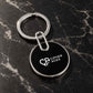 Black round custom logo keychain with silver metal ring and CIPHER ACES branding on a luxury marble surface