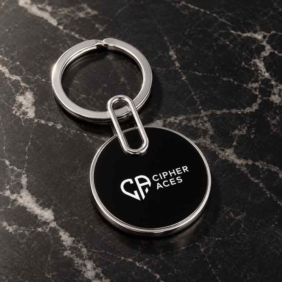 Black round custom logo keychain with silver metal ring and CIPHER ACES branding on a luxury marble surface