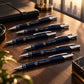 personalized ballpoint pens with gold custom logo detailing arranged in a fan-style display on a cream luxury tabletop, with an elegant gift box in the background, ideal for premium corporate gifting.