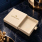 A cream-colored luxury gift box with its lid off, featuring a gold crown logo and the placeholder text 'YOUR LOGO'. The box is set on a dark blue marble countertop with gold-toned decorative accents in the background.
