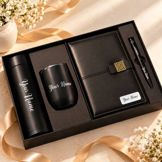Luxury personalized corporate gift set with black bottle, mug, leatherette diary and pen arranged diagonally on a simple ivory background with champagne-gold accents.