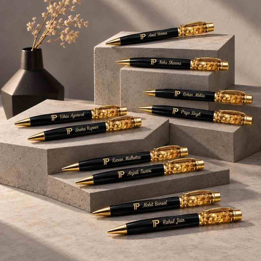 Personalized black pens with gold flake detailing and engraved names displayed on modern concrete pedestals in a minimalist luxury setting.