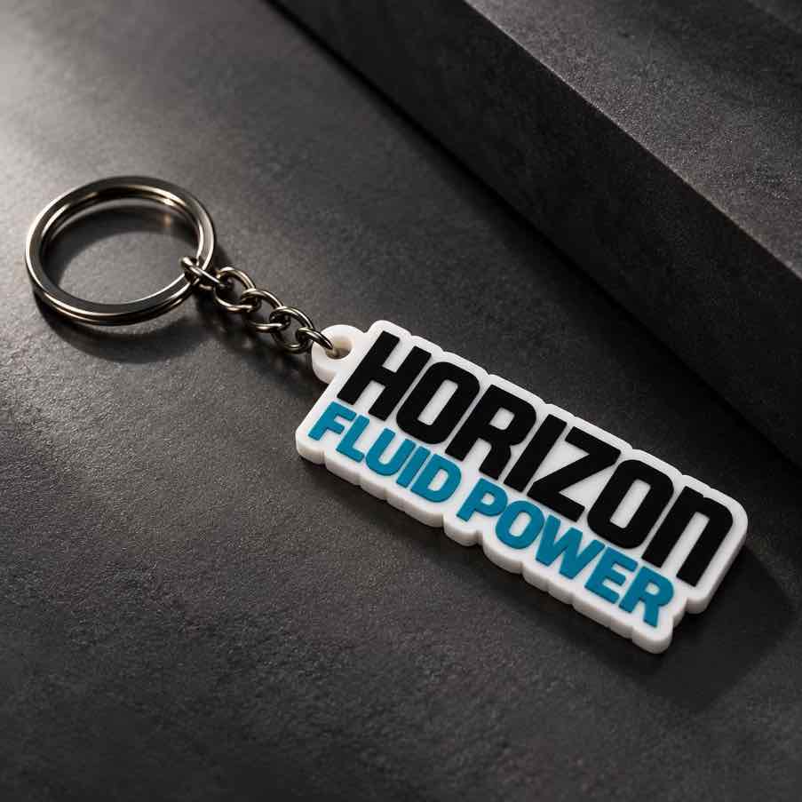 White Horizon Fluid Power personalized keychain with silver metal ring displayed diagonally on a dark textured surface