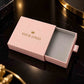A pink rectangular jewelry box with the lid partially open, showing a gray velvet interior. The lid is printed with a small gold crown icon and the words 'YOUR LOGO' in gold.