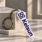 A custom white and purple rubber keychain with the name 'Kelsun' and a knot logo, resting on a textured stone block.