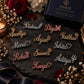 Gold, silver, and rose gold personalized name brooches arranged on a black stone surface with flowers and luxury ANKX packaging.
