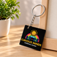 A square black acrylic keychain with a colorful logo and the text 'CURIOUS MINDS ChildCare Center' hangs from a silver metal ring on a wooden surface next to a potted plant.