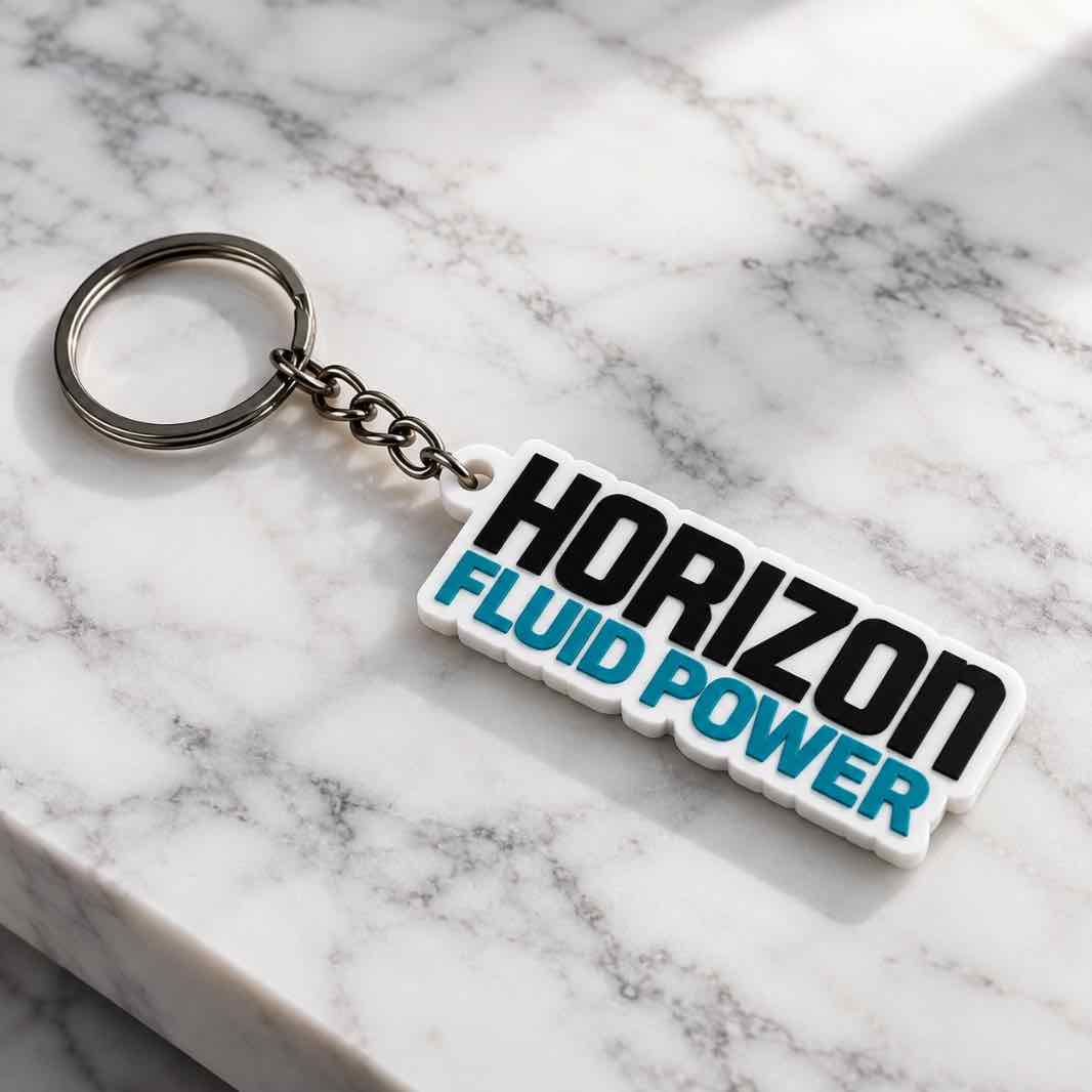 Custom Horizon Fluid Power acrylic keychain with black and turquoise lettering placed on a white marble surface with silver keyring
