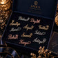 An open dark navy ANKX personalized jewellery gift box displaying multiple custom script nameplates in gold and rose gold tones on a black velvet insert. The box lid shows the ANKX logo and the words 'Personalised Jewellery'.