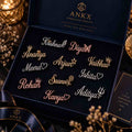 An open dark navy ANKX personalized jewellery gift box displaying multiple custom script nameplates in gold and rose gold tones on a black velvet insert. The box lid shows the ANKX logo and the words 'Personalised Jewellery'.