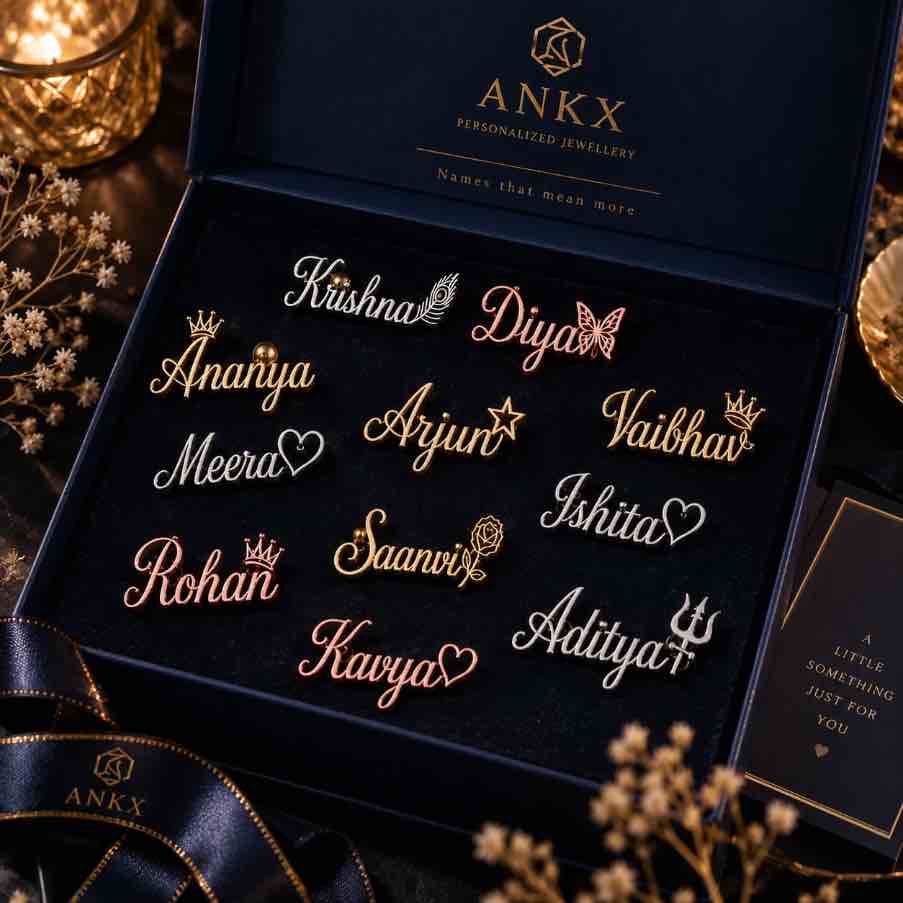 An open dark navy ANKX personalized jewellery gift box displaying multiple custom script nameplates in gold and rose gold tones on a black velvet insert. The box lid shows the ANKX logo and the words 'Personalised Jewellery'.