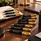 Custom black and gold engraved pens displayed on a walnut executive desk with a notebook and premium office accessories.