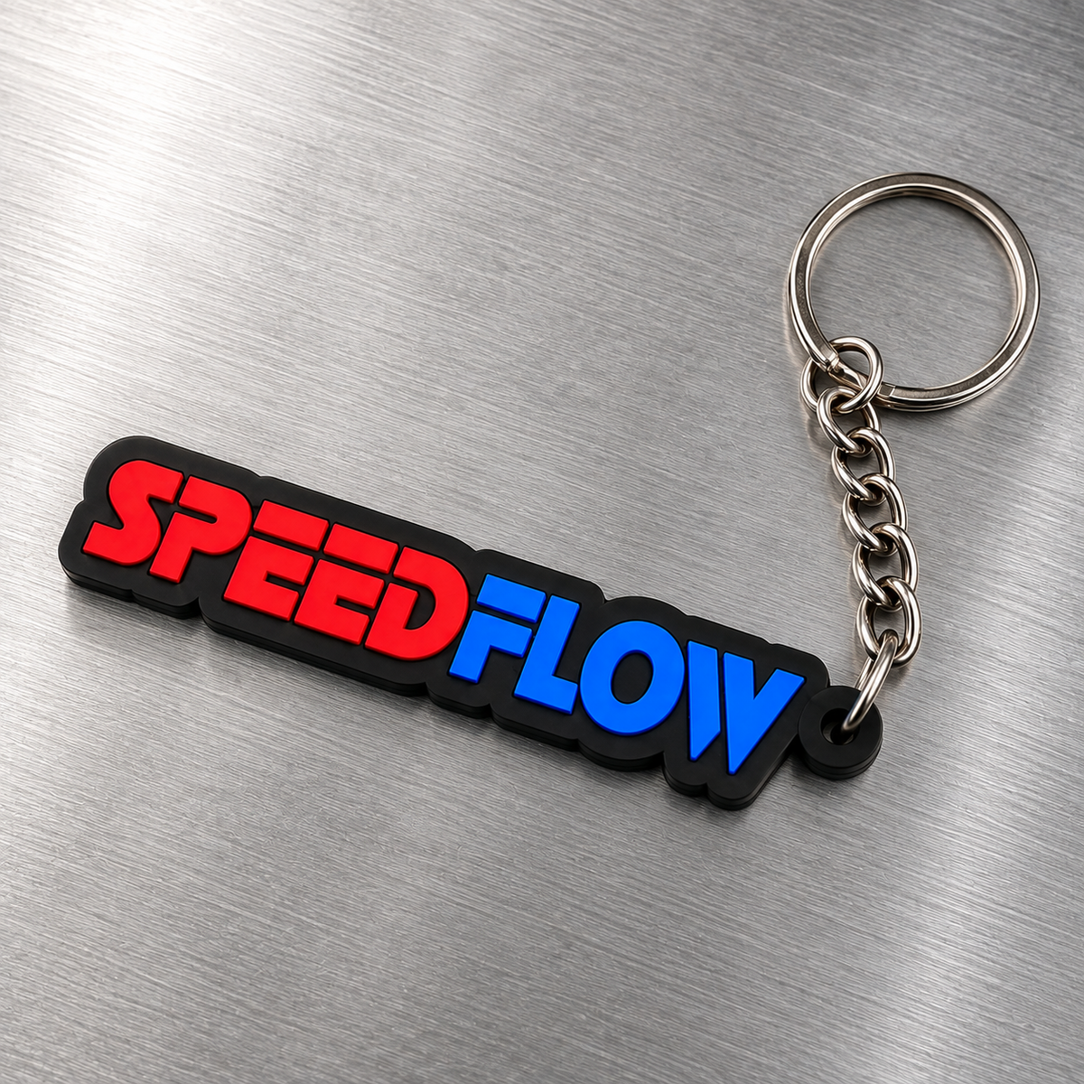A rectangular keychain with the words 'SPEEDFLOW' in red and blue lettering on a black background, attached to a silver metal split ring and chain, photographed on a brushed metal surface.