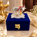 Silver cow and calf religious figurine with intricate detailing, red thread and gold bell, displayed on a royal blue velvet gift box with gold clasp.