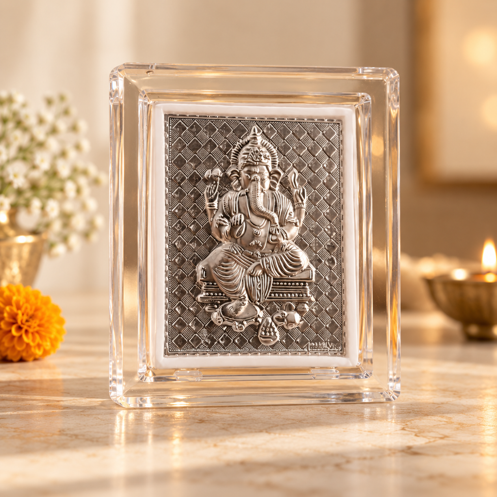 A square clear glass block plaque featuring a raised silver-toned relief of Lord Ganesha seated in the center, displayed on a marble surface with warm blurred background decor.
