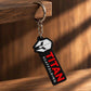 Titan Scaffolding keychain hanging from a wooden edge, featuring a black tag, white helmet icon, red TITAN lettering and silver metal keyring.