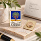 A rectangular enamel pin with a blue and gold palm tree design and the text 'ADNOC' in Arabic and English, displayed on a stone surface next to its gold-toned backing. The scene includes a notebook, pen, and decorative leaves in a styled tabletop setting.