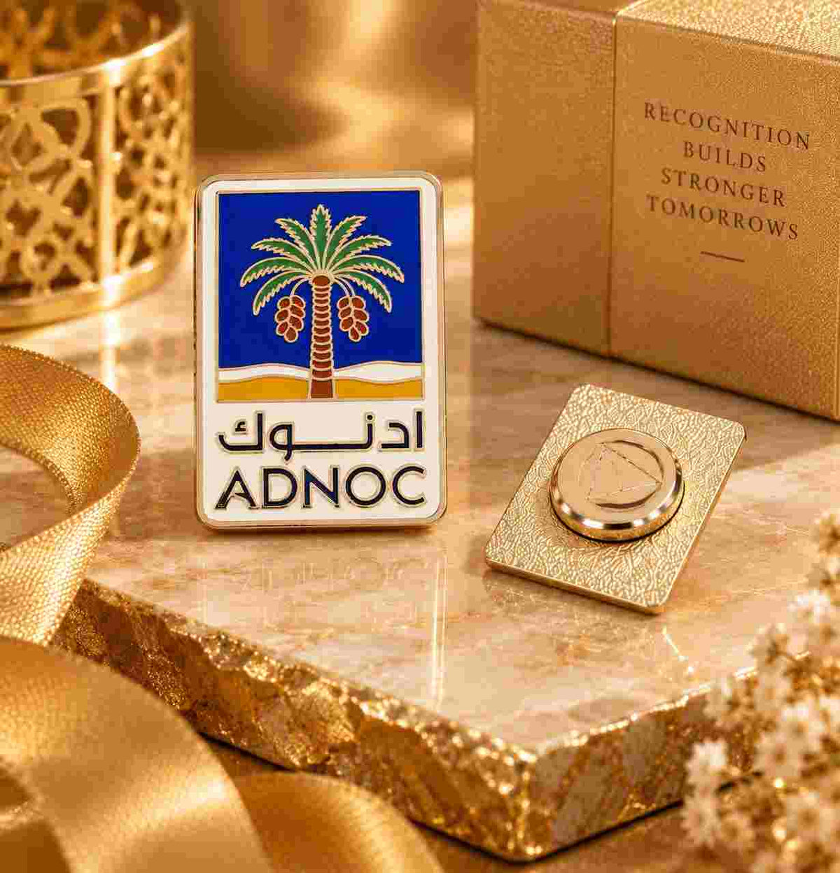 Personalized ADnoc logo lapel pin presented with a golden gift box and warm luxury-inspired styling.