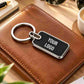 Personalized black metal keychain with silver trim and custom “YOUR LOGO” engraving, styled on a luxury leather notebook.