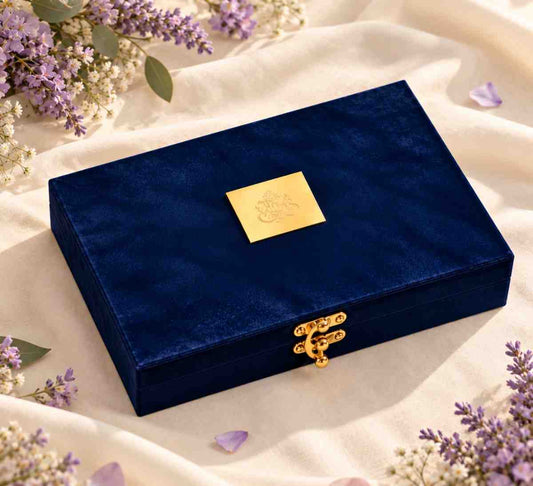 Dark navy blue velvet gift box with gold plaque and clasp on ivory fabric with lavender flowers