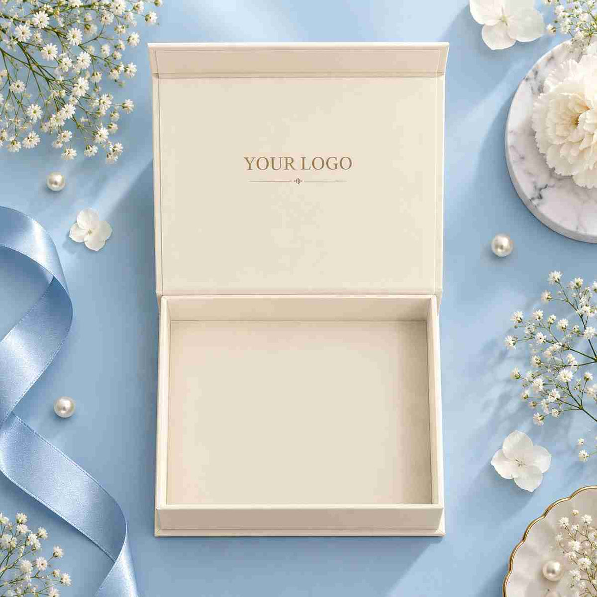 Open box, blue background Open cream gift box with custom logo inside the lid, displayed on a light blue background with ribbon and floral décor.