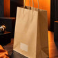 Large brown kraft paper carry bag showcased from a dramatic side angle against a charcoal and acid orange backdrop
