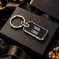 A customizable black rectangular keychain with a silver metal border, key ring, and split ring, displayed on a black gift box with a black ribbon.