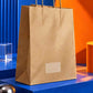 Brown kraft paper carry bag displayed from a front-left angle on a cobalt blue platform with vibrant orange accents