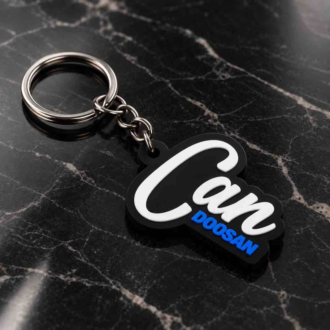 A black and white rubber keychain with the text 'Can DOGSAN' in white and blue, attached to a silver metal key ring, resting on a black marble surface.
